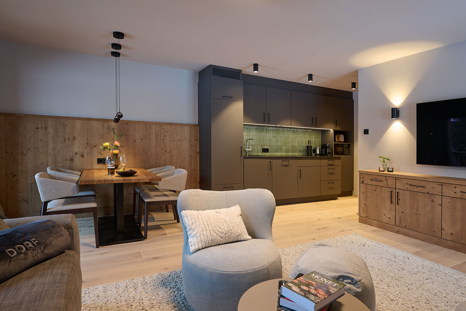 Offener Wohn- und Essbereich mit moderner Küche, Holzdetails, TV und gemütlichen Sitzmöbeln.