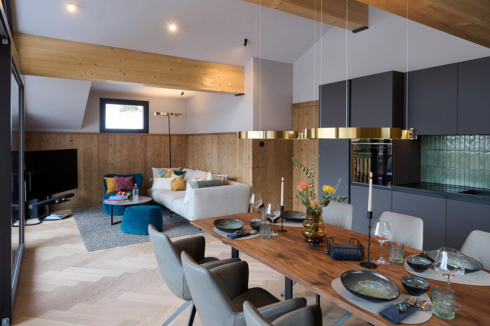 Moderne, schwarze Küche mit Essbereich, daneben Wohnbereich mit weißem Sofa, blauen Sesseln und TV.