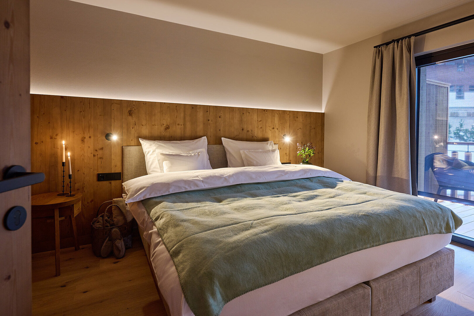 Modernes Schlafzimmer mit Holzverkleidung, großem Bett, Balkonzugang und stimmungsvoller Beleuchtung.