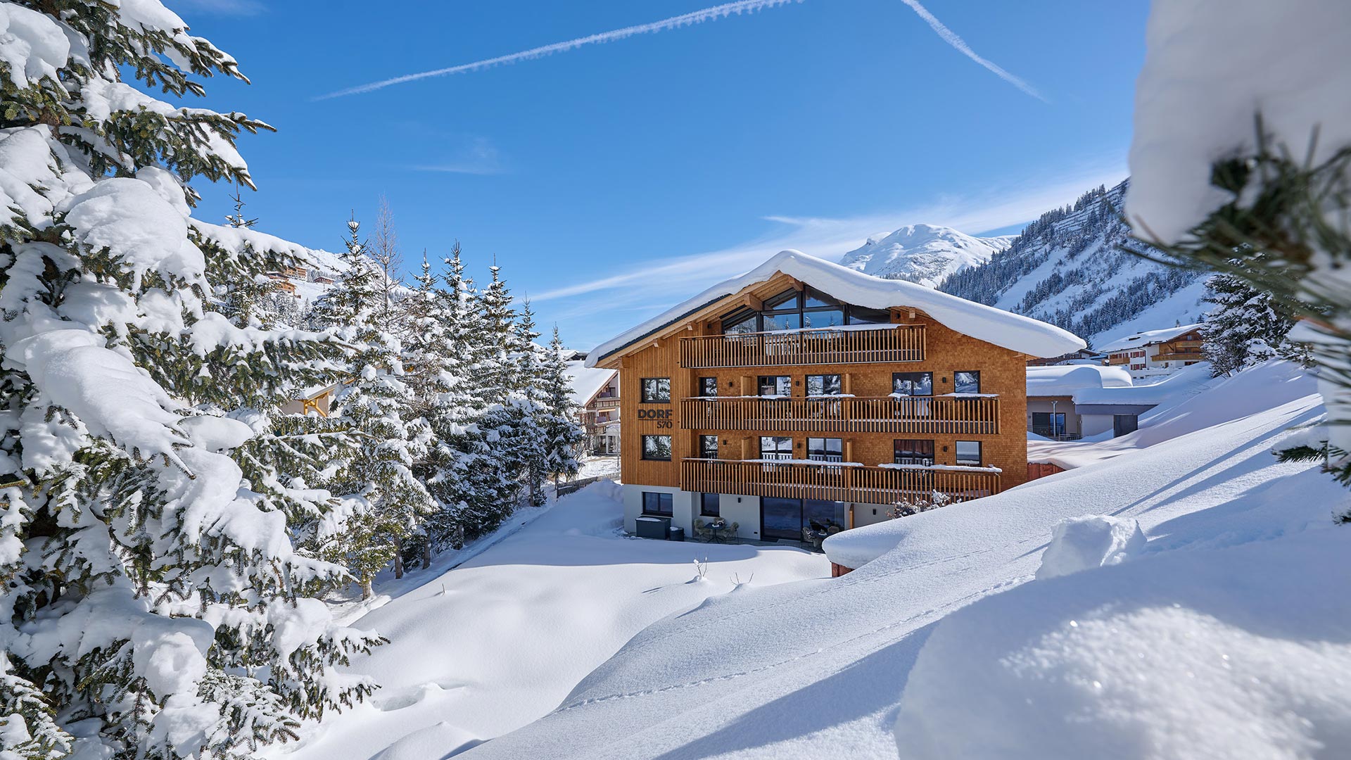 Außenaufnahme des Aparthotels Dorf570 im Winter bei Tag mit viel Schnee. Im Hintergrund schneebedeckte Berge.